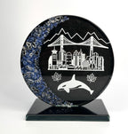 6 inch tall handcrafted circular glass award that has colored glass gems fused into the front of the award in the shape of a crescent moon. the award is painted metallic black on the reverse with etching of Vancouver landmarks, Canadian maple leafs and an orca killer whale. the award stands on a black glass base in front of a studio background