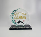 6 inch tall handcrafted glass award with colored glass gems fused into the front of the award in the shape of a crescent moon. the award has an multi colored etching of Vancouver landmarks, Canadian maple leafs and an orca killer whale. the award has a black glass base with clear glass gems fused into the base. the award stands in front of a studio background
