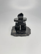 handcrafted 2.5 inch tall black granite inukshuk statue, on a chipped edge polished black granite base, with etching on the base. in front of a studio white background. 