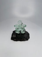 handcrafted 2.5 inch tall glass inukshuk statue, on a chipped edge polished black granite base, with etching on the base. in front of a studio white background. 