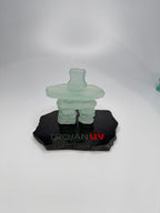 handcrafted 3.5 inch tall frosted glass inukshuk statue, on a chipped edge polished black granite base, with etching on the base. in front of a studio white background. 