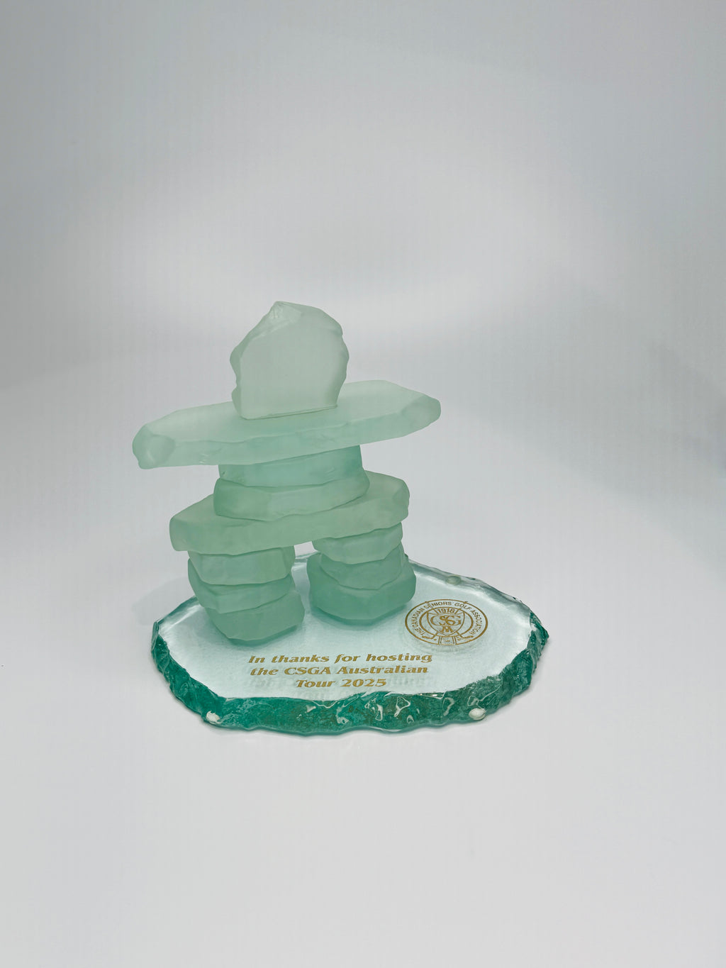 handcrafted 4.5 inch tall frosted glass inukshuk, on a clear icefloe glass base, with gold etching on the base. in front of a studio white background. 