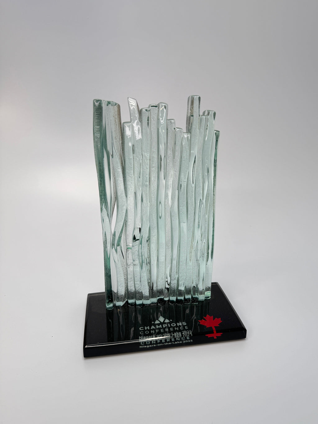 Glass Waterfall sculpture on a black base with 'Champions' and a maple leaf logo on a gray background