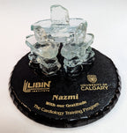 3 Clear Glass Inukshuks, Standing in a triangle formation. on top of a Black Painted glass base, with Gold etching Stating "Libin Cardiovascular institute" "University of Calgary" and "With our gratitude The Cardiology training program"