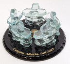 5 Clear Glass Handcrafted Inukshuks, standing in a circle, on top of a glass base that is painted black with gold etching stating "Calgary Alberta fall 2023"