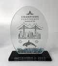 Glass award trophy with engraved design of a city skyline, bridge, and whale, on a black base.