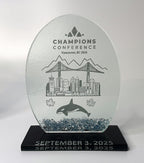 Glass award trophy with engraved design of a city skyline, bridge, and whale, on a black base.